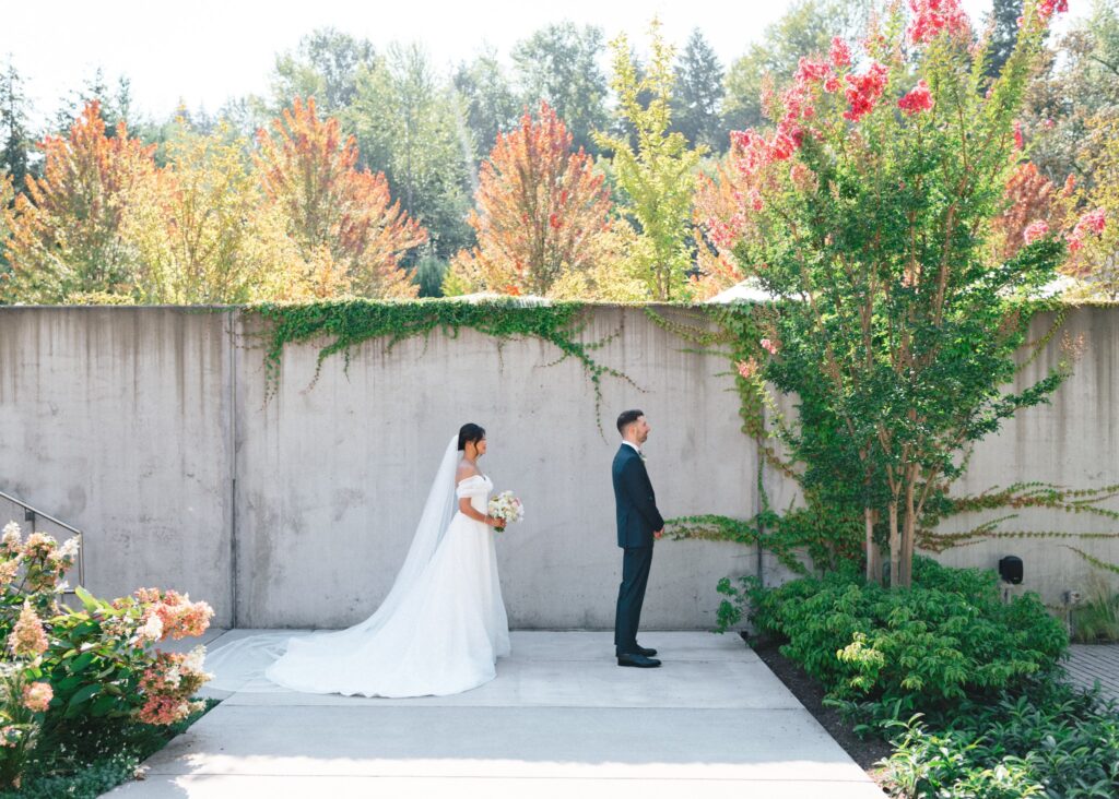 Bride walks up behind groom for their first look in Novelty Hill-Januik’s vine-draped courtyard.